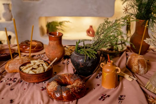 traditional table for a holiday. On the table, close-up, bread, loaf, plate with dumplings, clay pot with ears of corn and pine branches, beans on the tablecloth. in the background decorative wall