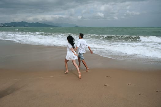 back of couple in love runs along the beach by the sea in summer on vacation
