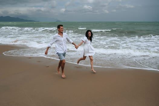 beautiful young couple in love runs along the beach by the sea in summer on vacation