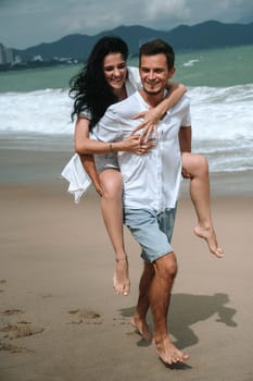 beautiful young couple in love runs along the beach by the sea in summer on vacation. Piggyback ride