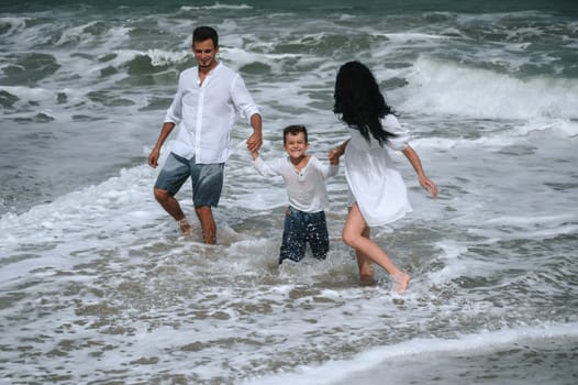 happy family parents with a child boy son playing on the beach in the sea on summer vacation