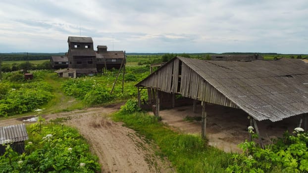 High angle weathered wooden farm buildings located in green field with dirt road in rural countryside in cloudy summer day