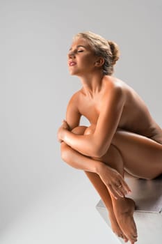 Nude blonde sitting on the cube profile view