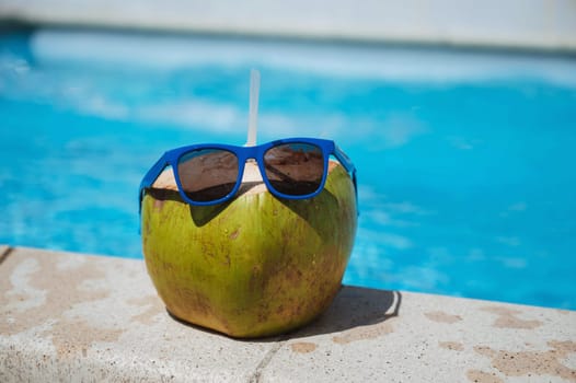 drinking coconut with a straw in sunglasses relax by the swimming pool at the resort in the hotel in summer