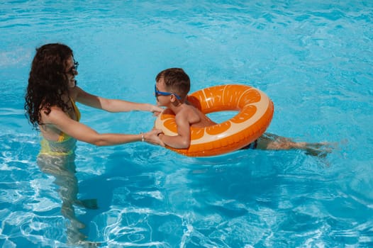 young mother teaches her child boy son to swim in swimming pool at a hotel on vacation at a resort in the summer