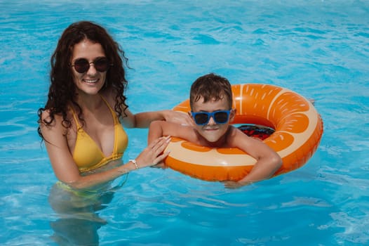 happy young mother teaches child boy son to swim in swimming pool at a hotel on vacation at a resort in the summer