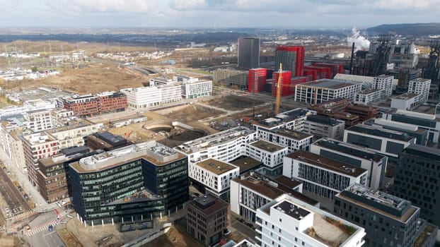 High-angle aerial view of Esch-sur-Alzette, Luxembourg, showcasing modern residential and commercial buildings, ongoing construction, and the integration of historic industrial sites.