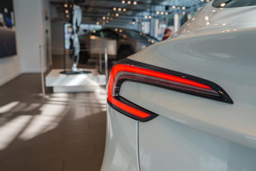 A sleek car with unique red taillights is displayed in a bright showroom. The polished floor and contemporary decor enhance the vehicle's glossy finish.