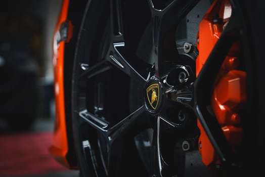 Detailed view of a Lamborghini Revuelto wheel featuring a black alloy rim and orange brake caliper. The iconic emblem is centered, with a blurred background.