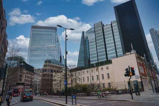A vibrant London street scene featuring modern skyscrapers like the Leadenhall Building alongside historic architecture, under a partly cloudy sky.