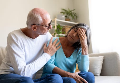 Mature man consoling sad wife sitting on the sofa at home living room. Mental health concept.