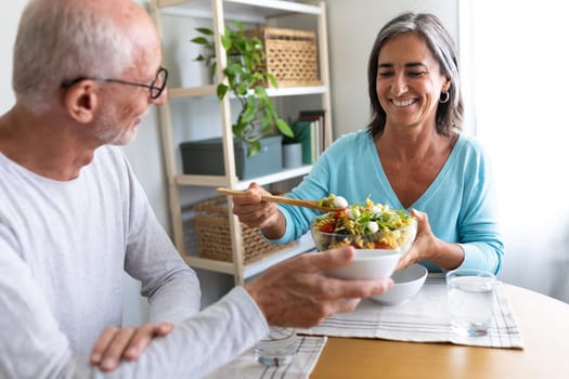 Woman serving pasta salad to husband. Mature married couple having meal together at home dining table. Lifestyle concept.