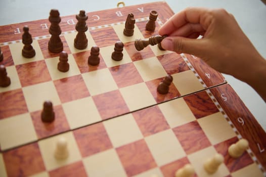 An individual's hand holding a chess piece on a wooden board during a game, symbolizing strategy and focus.