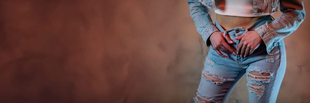 A stylish woman is showcasing her trendy distressed jeans and a cropped jacket against a striking textured backdrop