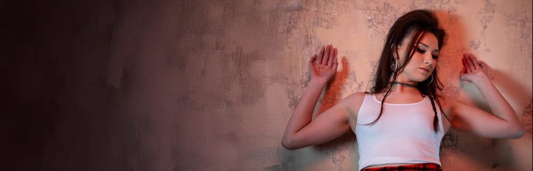 A young woman in casual attire poses gracefully against a textured wall, showcasing fashion and mood.