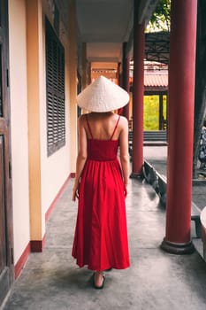 back of a beautiful woman traveler in a dress and a traditional Vietnamese hat at a pagoda in Vietnam on a travel to Asia