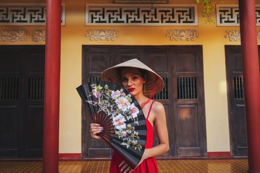 beautiful young woman tourist with a fan in a Vietnamese traditional non la hat at pagoda on trip in Nha Trang in Vietnam in Asia