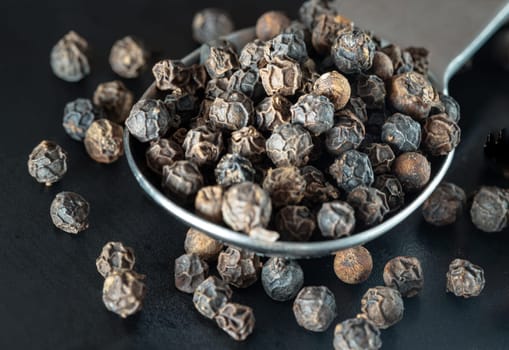 Raw organic black peppercorns or Dry black pepper seeds in stainless steel spoon on black background. use it as your Space for text, Design, Wallpaper and Poster, Selective focus.