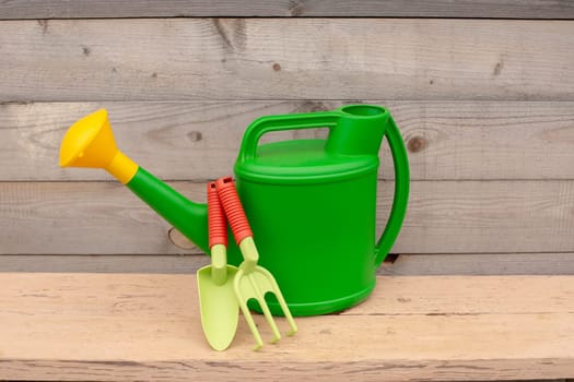 Set from green and orange hands tools , watering can stand on wooden background. Copy space. Close up