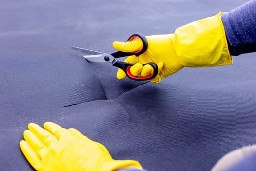 Step by step. Instructions for planting pepper seedlings on spunbond. Hands in yellow gloves cut out a seedling hole. Step 1