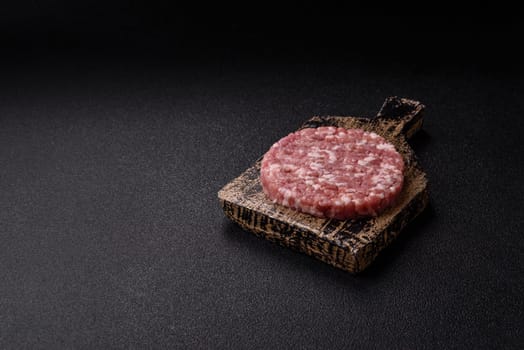 Fresh raw ground beef or pork burger patty with salt and spices on textured concrete background