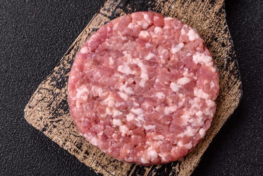 Fresh raw ground beef or pork burger patty with salt and spices on textured concrete background