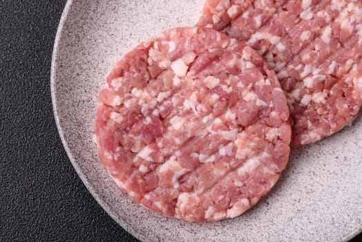 Fresh raw ground beef or pork burger patty with salt and spices on textured concrete background