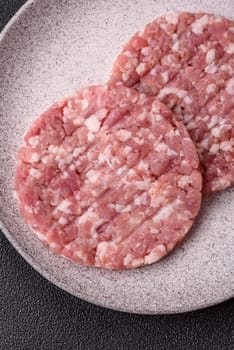 Fresh raw ground beef or pork burger patty with salt and spices on textured concrete background