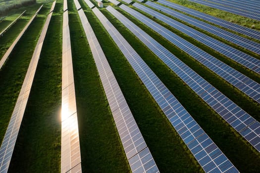 From above drone view of sunlight reflecting on solar panels arranged on vast agricultural field. The farmland is equipped with renewable energy generators during daytime