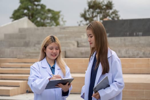 Two diverse female doctors reviewing notes together outside a healthcare facility, emphasizing collaboration and attention to detail in patient care.