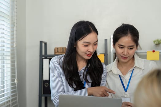 A diverse business team of two women engaging in a discussion while pointing at a laptop screen in a collaborative office environment.