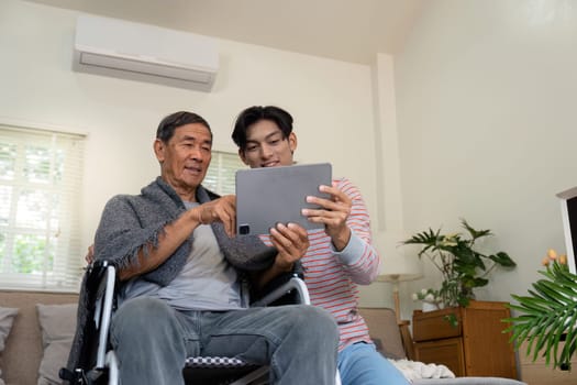 A joyful son shows something on a tablet to his elderly father in a wheelchair, celebrating family connection and technology in a warm home atmosphere.