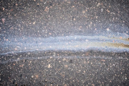 A vibrant oil slick stretches across the asphalt, reflecting various colors in the sunlight. This striking sight captures the interplay of light and pollution in the urban landscape