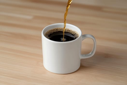 Close-up of hot black coffee being poured into a white cup on a wooden surface..