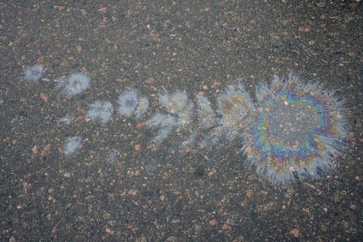 Colorful gasoline or oil spill creating a rainbow pattern on asphalt road, indicating pollution and environmental damage.