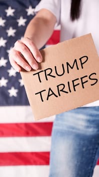 Unrecognizable woman holding sign with text Trump Tariffs against American flag on background