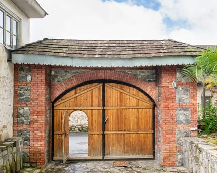 The wooden entrance of Imam Ali Mosque in Shaki, Azerbaijan, comprises a wooden arched door flanked by stone walls and adorned with greenery