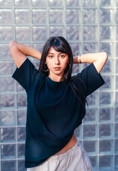 A young woman stands confidently in a minimalistic studio, her long dark hair held back as she poses with a focused expression. Natural light enhances the moment's simplicity.