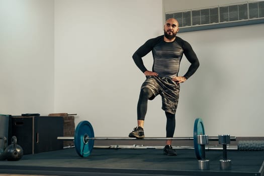 A male athlete demonstrates strength training in a fitness studio, standing on one leg while balancing over a barbell. Various weights are placed around him, showcasing a dedicated workout.