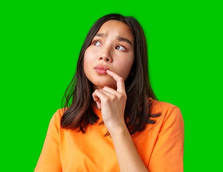 A young woman with long dark hair poses thoughtfully against a vibrant green backdrop. She rests her finger on her chin, indicating deep thinking or curiosity.