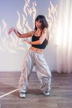 A dancer showcases her skills in a stylish outfit featuring baggy pants and a crop top. The room has artistic lighting that creates a dynamic atmosphere, enhancing her movements.