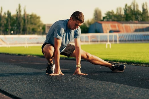 A young athlete performs a dynamic stretch on a track field at a sports facility during the evening. The sun sets, creating a warm glow and enhancing the training atmosphere.