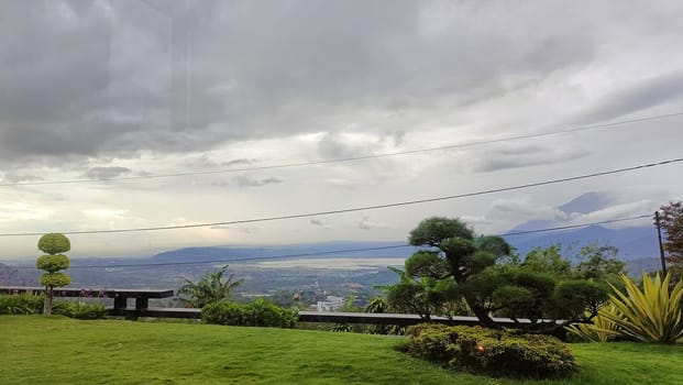 Serene hillside view featuring lush greenery, carefully shaped trees, distant mountains, and an overcast sky conveying tranquility in nature.