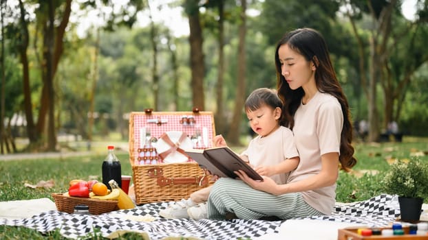 Loving mother and son reading a book during picnic in the park. Outdoor leisure and family bonding concept.