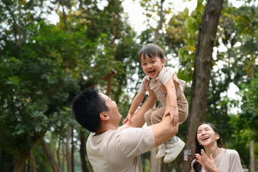 Happy father lifting his laughing son in the air. Outdoor leisure and family bonding concept.