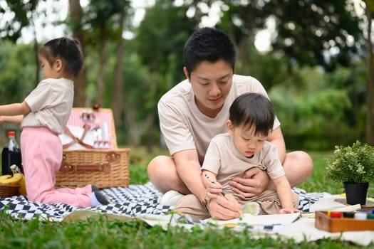 Loving father and little boy painting together during picnic in the park.