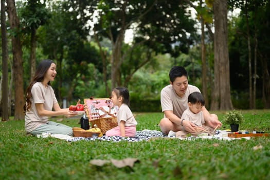 Happy family with two little children enjoying a picnic on a beautiful day in a park.