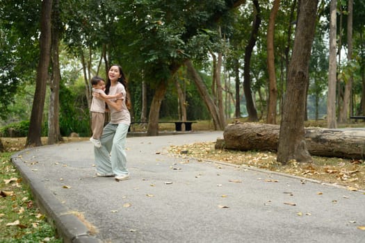 Loving mother playing with her little son on a walking path in a beautiful park.