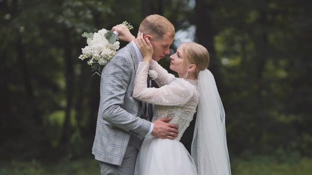 Loving newlyweds hugging among trees, white flowers in hand, sharing intimate moment during woodland wedding celebration