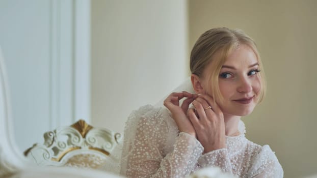 Beautiful bride adjusting delicate earrings, elegant white gown highlighting wedding day beauty and anticipation